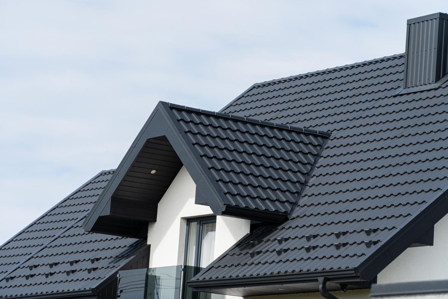 Black metal roof on a white house, chimney, and gray sky.